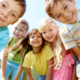 a group of kids huddle around a camera outside on a sunny day