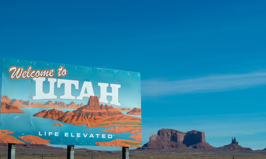 Rocky desert area in the background of a sign that displays "Welcome to Utah"