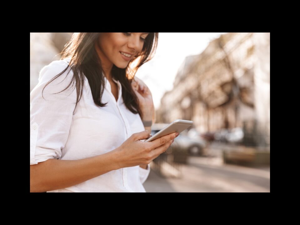 a woman with long brown hair outside looks at her phone